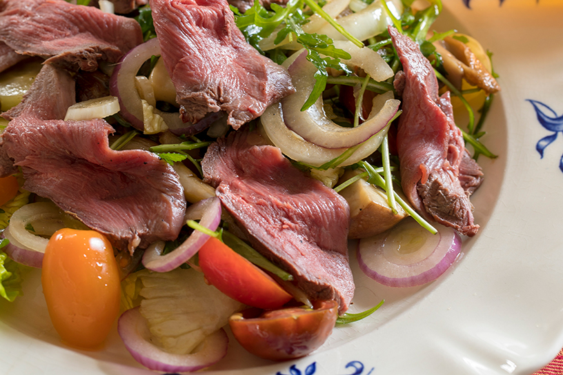 carpaccio van gans met rode ui, rucola en hazelnoten op een bord